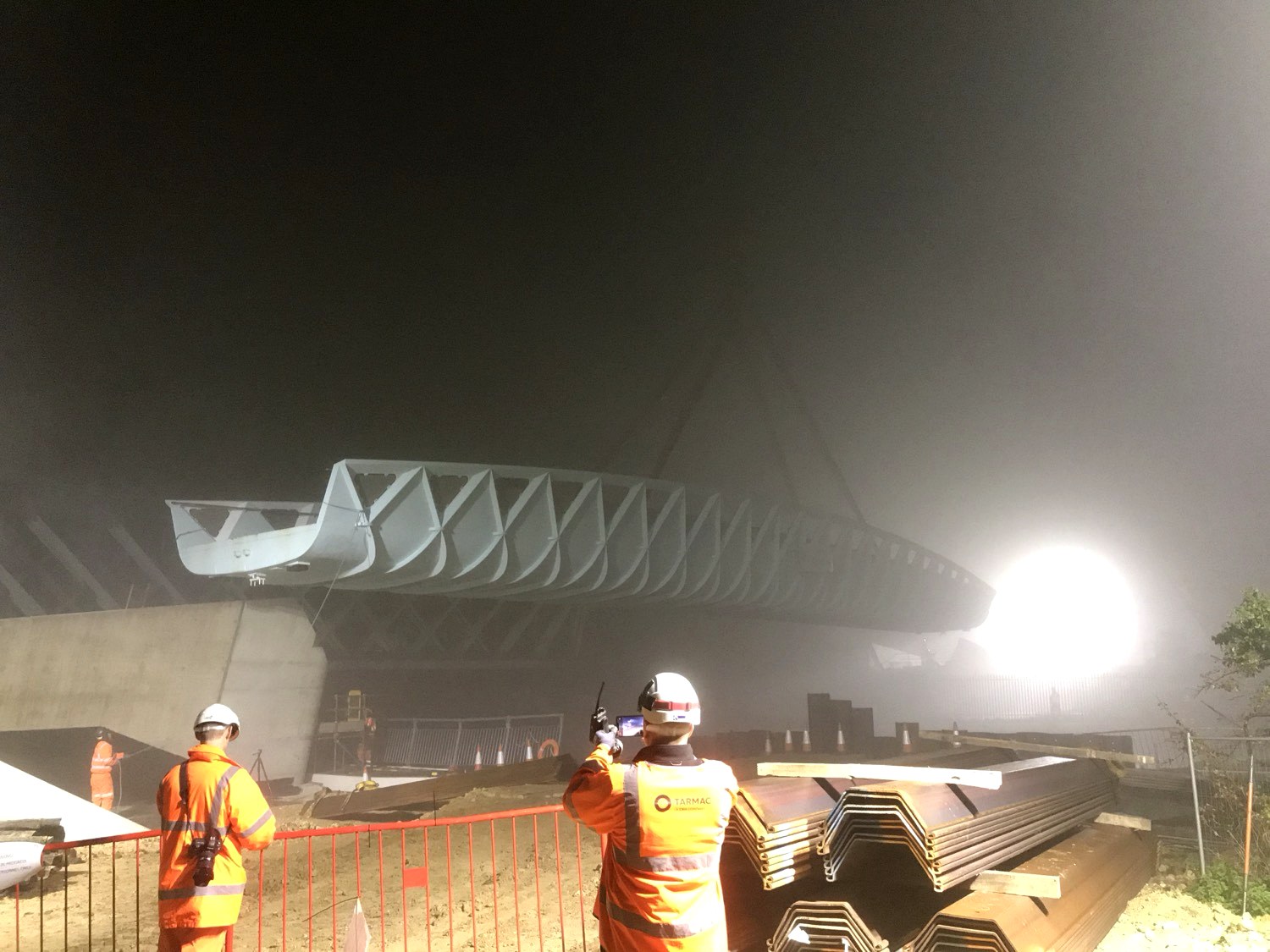Steel bridge span being lifted onto a concrete abutment at night